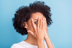 Portrait of young scared afraid frightened african girl cover face with hands stressed isolated on blue color background