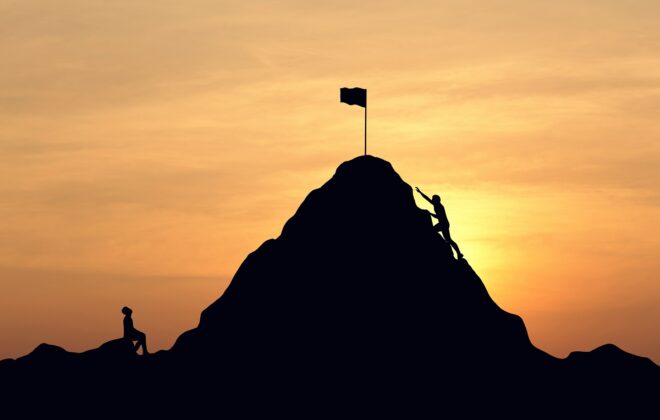 Silhouette of teams trying to scale a mountain at sunset