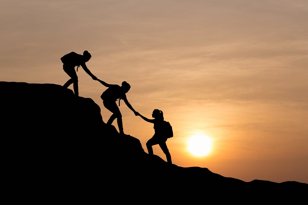 Silhouette of people helping each other hike up a mountain