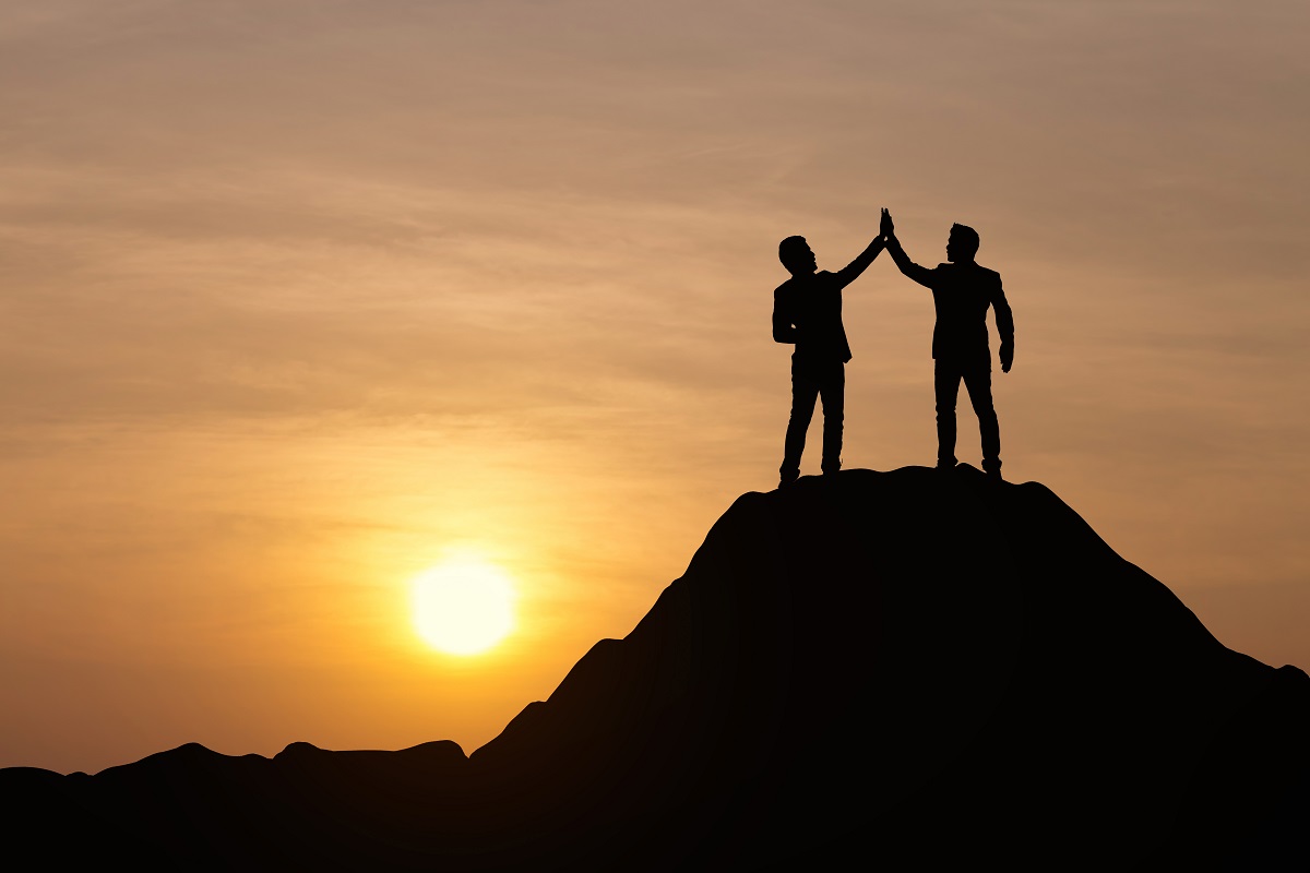 Silhouette of people celebrating success at top of mountain