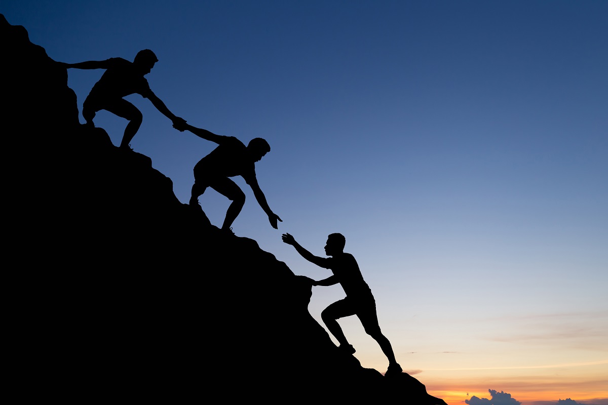 Silhouette of people helping each other hike up a mountain