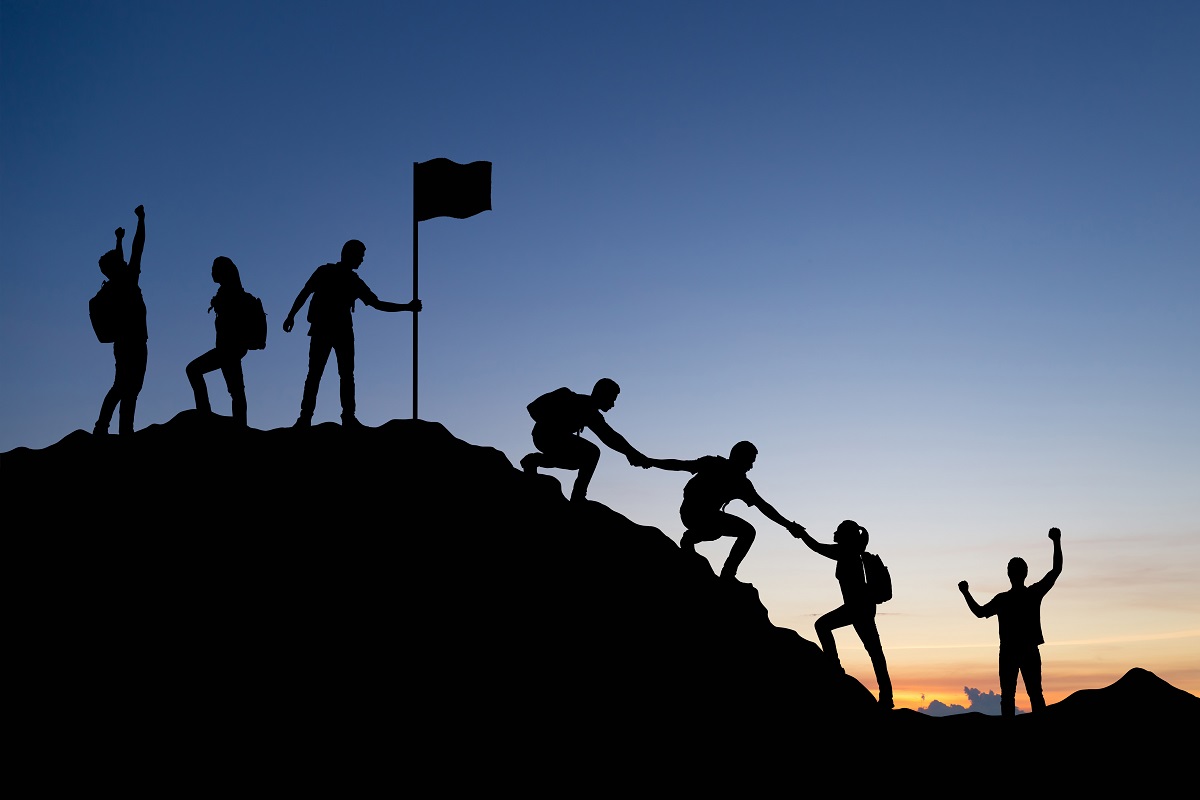 Silhouette of people helping each other hike up a mountain